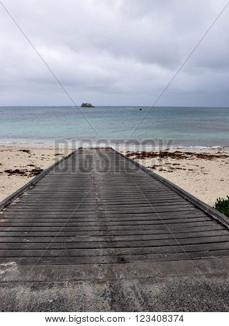 Boat ramp launch into the turquoise Indian Ocean waters at Hamelin Bay beach under dark, stormy skies in Western Australia.