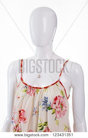 Sarafan with pendant on mannequin. Female mannequin in light dress. Floral clothing and small accessory. Casual garment with expensive jewelry.