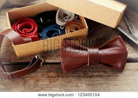 Brown leather bow tie and full cardboard gift box of ties on wooden table, close up
