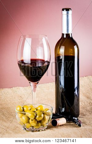 glass of red wine and its bottle, with olives and corkscrew