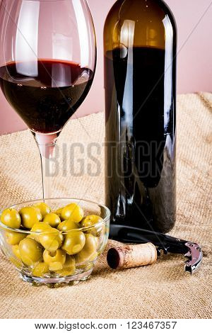 glass of red wine and its bottle, with olives and corkscrew
