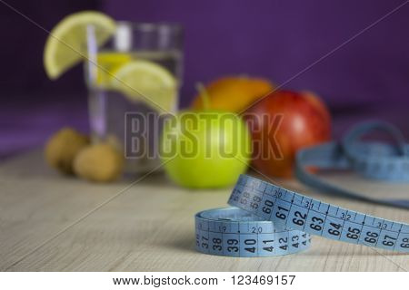 meal for loss weight and good health - fresh lemon water in glass and green & red & orange fruits behind tape for measuring