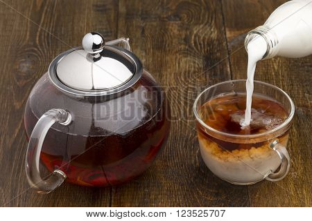 Set of glass teapot cup and bottle of milk on wooden table