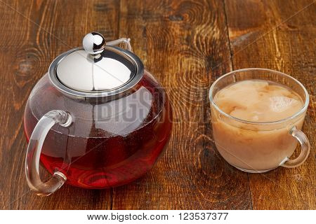 Set of glass teapot and teacup of black tea with milk on wooden table