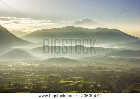 foggy morning view of volcan Cayambe en ecuador at sunrise with colored hills and sun rays