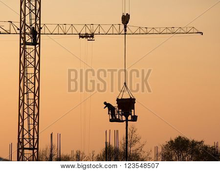 Silhouette of construction worker on the crane at sunset