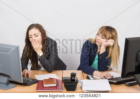 Two Young Office Employee Wearily Sitting Behind A Desk