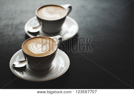 Two cups of cappuccino with latte art on black table. Morning coffee for couple in love. Top view.