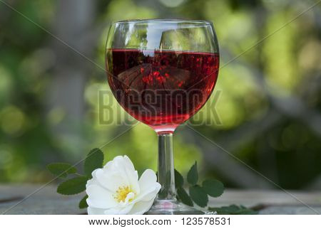 a glass of red wine and a white rose
