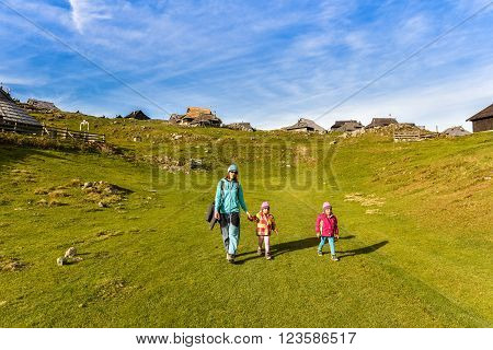 Family hiking in the mountains on idyllic meadow on Velika Planina Slovenia. Mother and two twin children are hiking on the foot path in the nature in alps and hills. Active family .