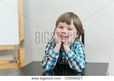 Blond boy sitting at the table at home and learns. The idea of school school home education and developmental activities.