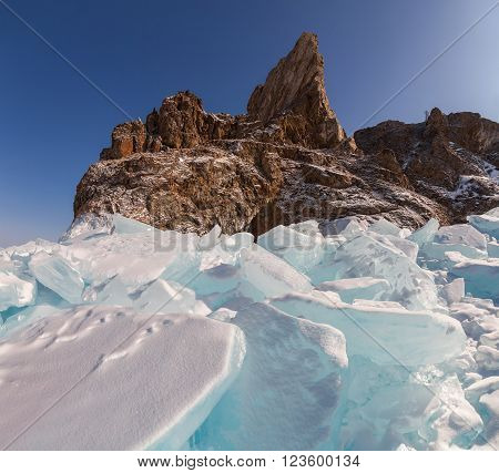 Big parts of breaking ice of The Baikal Lake in winter. High rock Khoboy on the coast