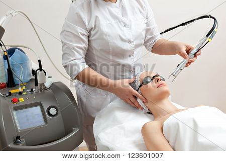 Woman lying on a table with protect glasses on eyes getting a laser skin treatment in healthy beauty spa salon