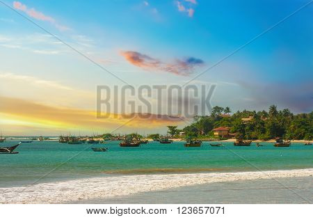 Beautiful sunrise tropical beach white sand turquoise ocean water . Boats of fishermen on the water. Palm trees and tropical vegetation on the coast.