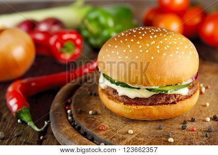 Classic american burger food. Hamburger at wood. Wooden desk with hamburger and fresh vegetables composition. Burger with cheese, beef, cucumber, lettuce. Cheeseburger at wooden background.