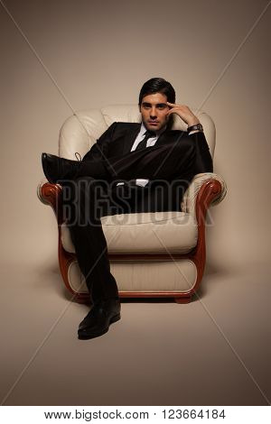 Confident successful young handsome man businessman in elegant suit with tie on armchair . Manhood. Male Beauty. Fashion model studio shoot . Italian Style