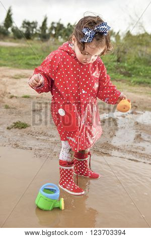 Baby girl dressed with dotted raincoat and rainboots playing with her sprinkling can