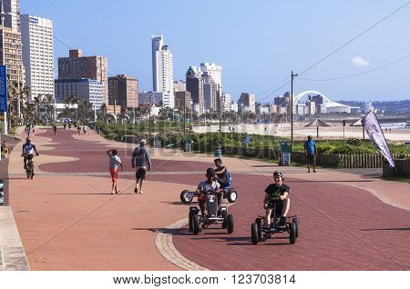 DURBAN SOUTH AFRICA - MARCH 23 2016: Many unknown people walk and ride along paved promenade on Golden Mile beachfront against city skyline in Durban South Africa