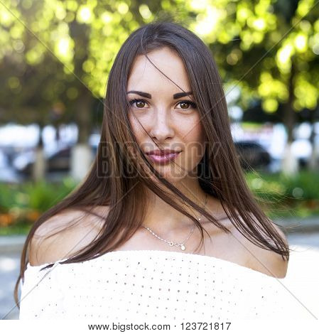 Beautiful girl portrait, close-up brunette in a white blouse, fashion style urban life, a bright sunny summer day. In the open air. Sensually looking eyes.