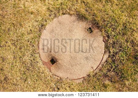 Concrete Manhole Cover Drainage System In The Midst Of Cropped Dry Grass