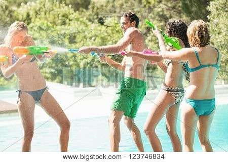 Happy friends doing water gun battle near swimming pool