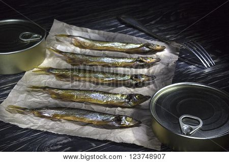 Smoked capelin and conserve tins on dark wooden background