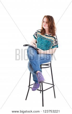 Beautiful smiling redhead plus size wreckled model with folder and ballpoint pen sitting on the bar chair. Isolated on a white background.