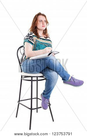 Beautiful smiling redhead plus size wreckled model with folder and ballpoint pen sitting on the bar chair. Isolated on a white background.