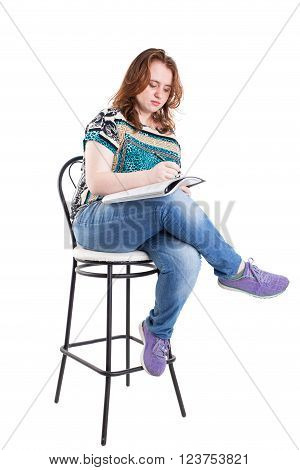 Beautiful smiling redhead plus size wreckled model with folder and ballpoint pen sitting on the bar chair. Isolated on a white background.