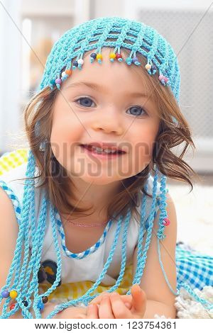 Little girl wearing a blue hat on a furry white carpet