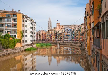 Colorful yellow and orange houses and bridge Pont de Sant Agusti reflected in water river Onyar, in Girona, Catalonia, Spain. Church of Sant Feliu and Saint Mary Cathedral at background.