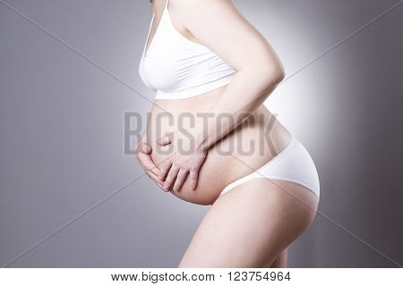 Caucasian pregnant woman in white lingerie with abdominal pain on gray studio background. Pregnancy concept