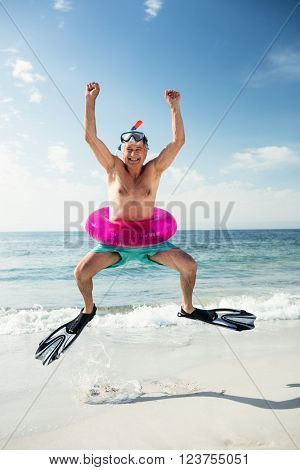 Portrait of senior man in inflatable ring and flippers jumping on beach on a sunny day