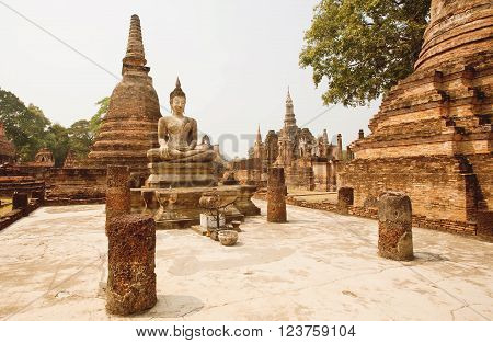 Brick pagoda and ancient ruined columns of temple Wat Maha That with Buddha statue at Sukhothai historical park. UNESCO World Heritage Site.