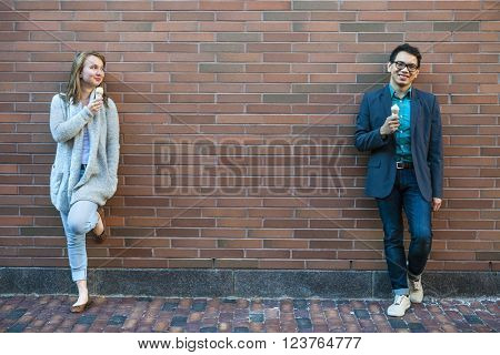 Two smiling young people holding ice cream cones standing apart near brick wall with copy space