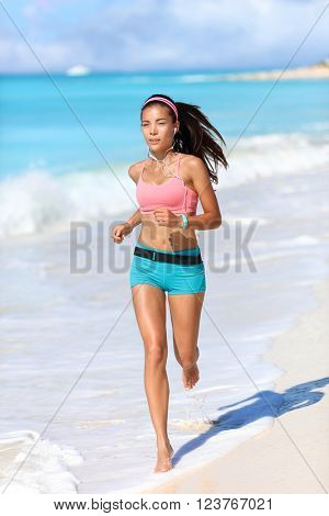 Fitness running runner exercising cardio with smartwatch activity tracker jogging barefoot on white sand beach living an active healthy lifestyle. Asian fit woman with wearable tech.