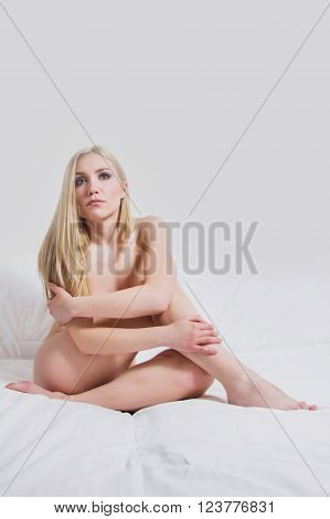Young sexy nude girl sitting on the bed, emotive expression, looking alone and sad