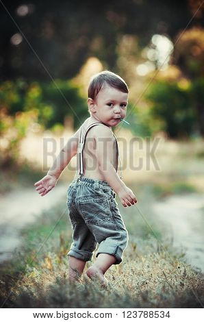 Little boy holds in his mouth lollipop on a stick outdoors and smiling