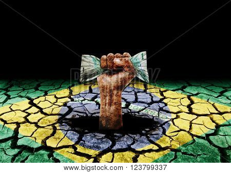 degraded hand holding money coming out of hole in painted cracked ground with the flag of Brazil
