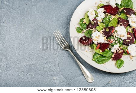 Salad with roasted beetroot, spinach, soft goat heese and seeds in light plate over grey concrete textured background. Top view, copy space
