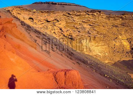 Red volcanic rocks with tourist shadow in El Golfo bay on Lanzarote island in Spain