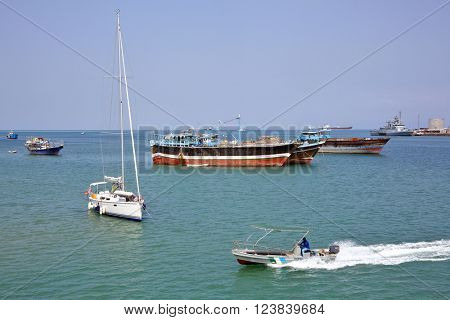GULF OF ADEN, DJIBOUTI - FEBRUARY 08, 2016: Coast Guard boat goes by luxury sailing boat, fishing and cargo ships at anchor in the port of Djibouti