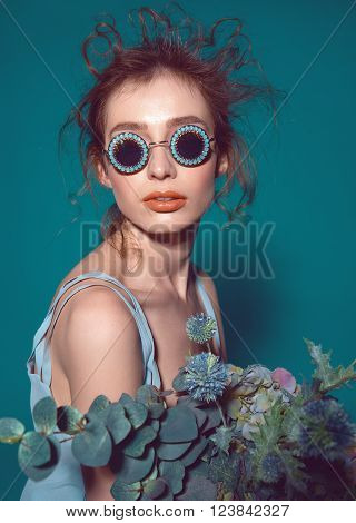 Beautiful fashion hipster in vogue sunglasses and flowers bouqet . model woman with professional make up and hairstyle on blue background . photo