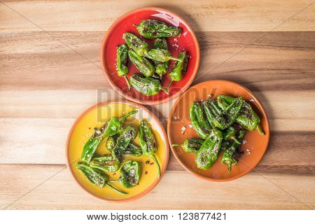Grilled padron peppers with salt and pepper on colourful plates top view