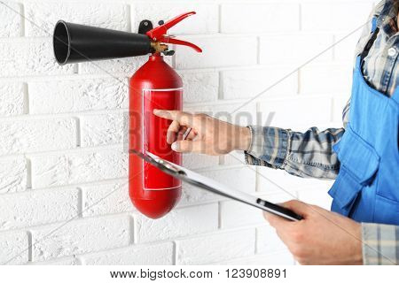 Man inspecting the fire extinguisher against white brick wall background