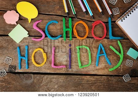 Inscription SCHOOL HOLIDAY made of colorful plasticine and stationery on wooden background