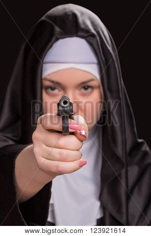 Beautiful nun aiming a gun at the camera blurred isolated on a black background