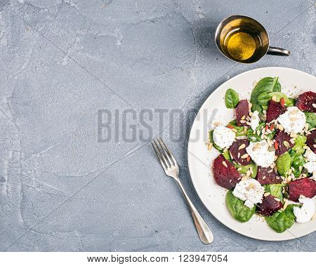 Salad with roasted beetroot, spinach, soft goat heese and seeds in light plate over grey concrete textured background. Top view, copy space