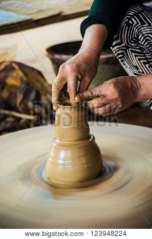 Closeup view of hands of a senior asian potter forming clay into a pot on a turntable. Image of asian handcrafts and manuafacture.