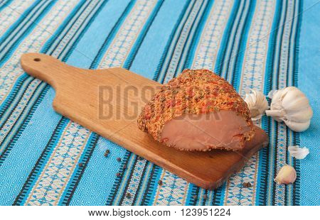 A piece of meat balyk with a crust of spices and sesame seeds on a cutting board